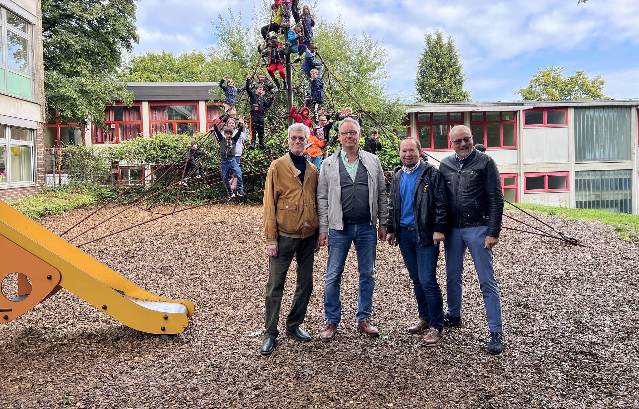 In Hintergrund testen die Kinder das neue Klettergerüst. IM Vordergrund, von links: Dieter Jünemann von den Rotariern, Schulleiter Dirk Breuer sowie Lothar Kluba und Joachim Wendel von den Rotariern. 