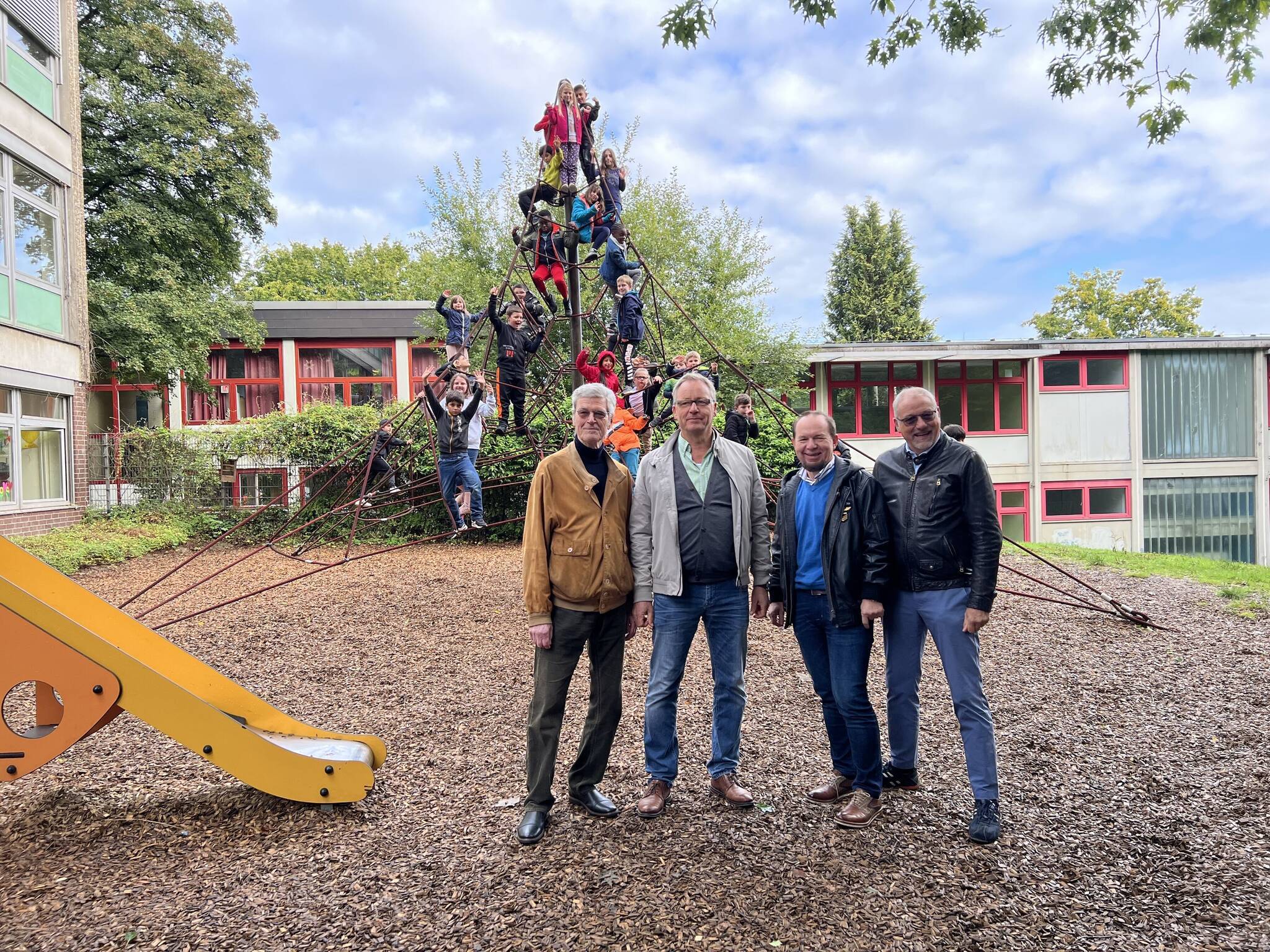 In Hintergrund testen die Kinder das neue Klettergerüst. IM Vordergrund, von links: Dieter Jünemann von den Rotariern, Schulleiter Dirk Breuer sowie Lothar Kluba und Joachim Wendel von den Rotariern. 