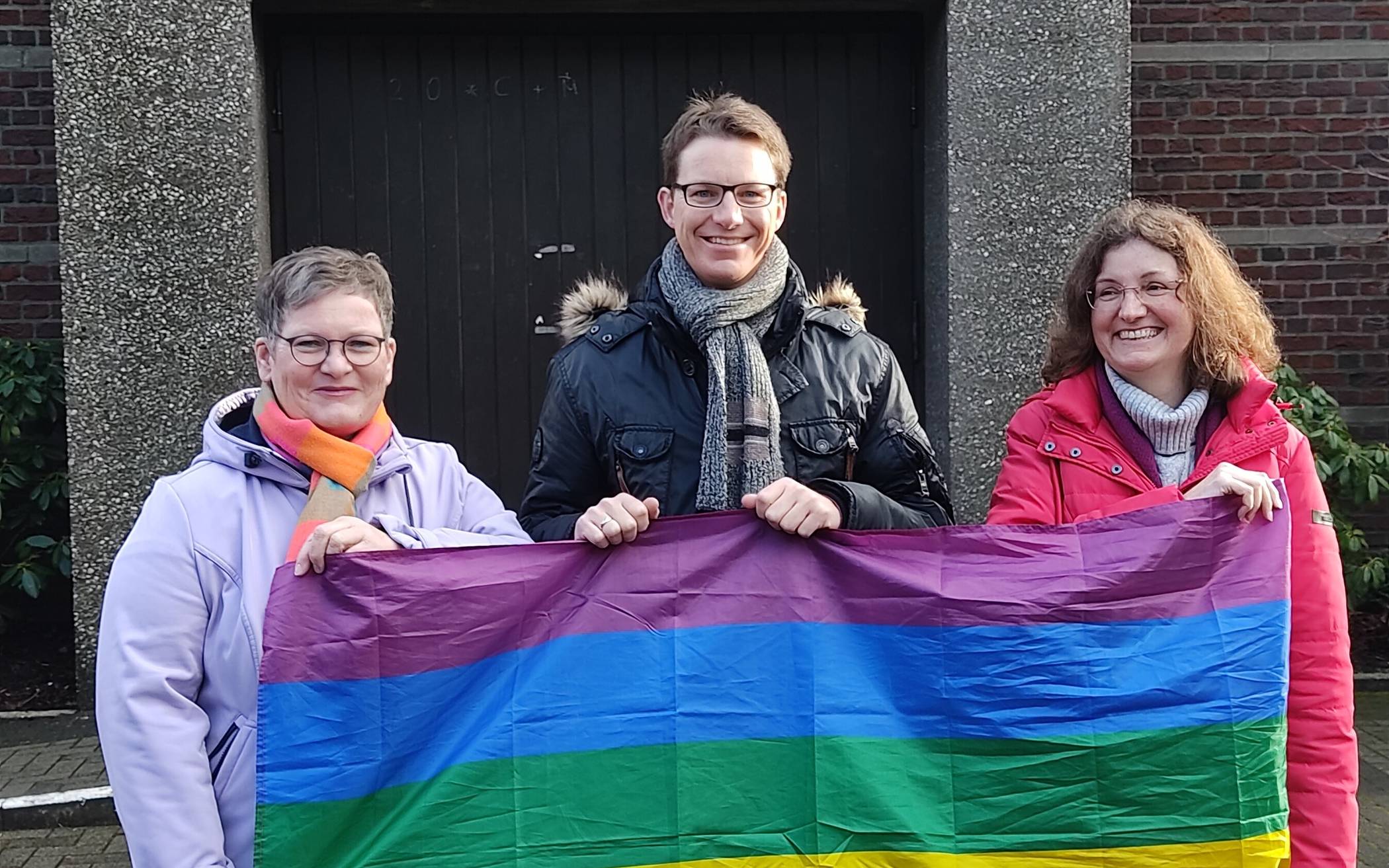 Andrea Lauer, Maximilian Bröhl und Petra Hermes-Wigge mit der Regenbogenflagge. 