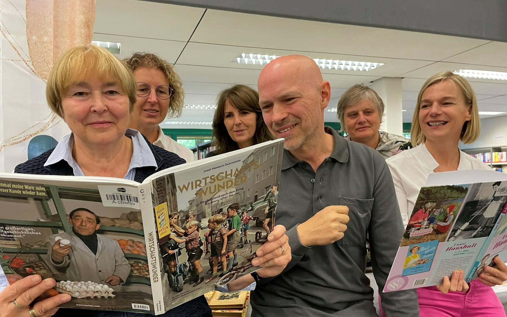 Von links: Gisela Bendt, „Aule Mettmanner“, Bürgermeisterin Sandra Pietschmann, Gabriele von Mauschwitz, Alzheimer Gesellschaft Kreis Mettmann, Oliver Pahl, Wohn- und Pflegeberatung der Stadt, Ursula Leifeld, Leiterin der Stadtbibliothek, und Petra Brinkmann-Schepke, Wohn- und Pflegeberatung der Stadt, schauen sich Bücher über die 1950er-Jahre an. 