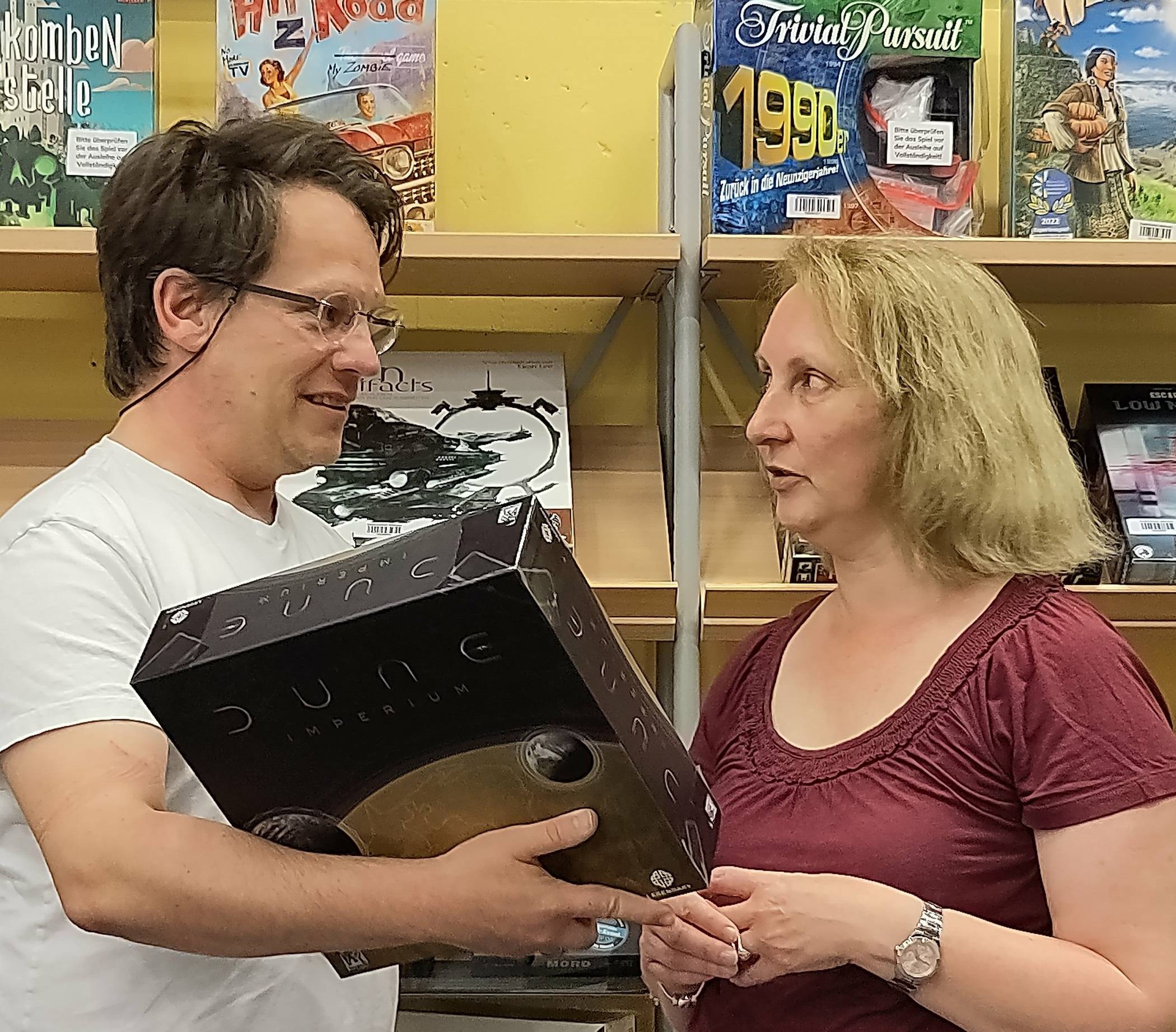  Martin Koch (2. Vorstand Freundeskreis) erklärt Andrea Perry (ebenfalls Vorstand Freundeskreis) sein aktuelles Lieblingsspiel Dune im neuen eröffneten Bereich „Spiele ab 12 Jahren“.    