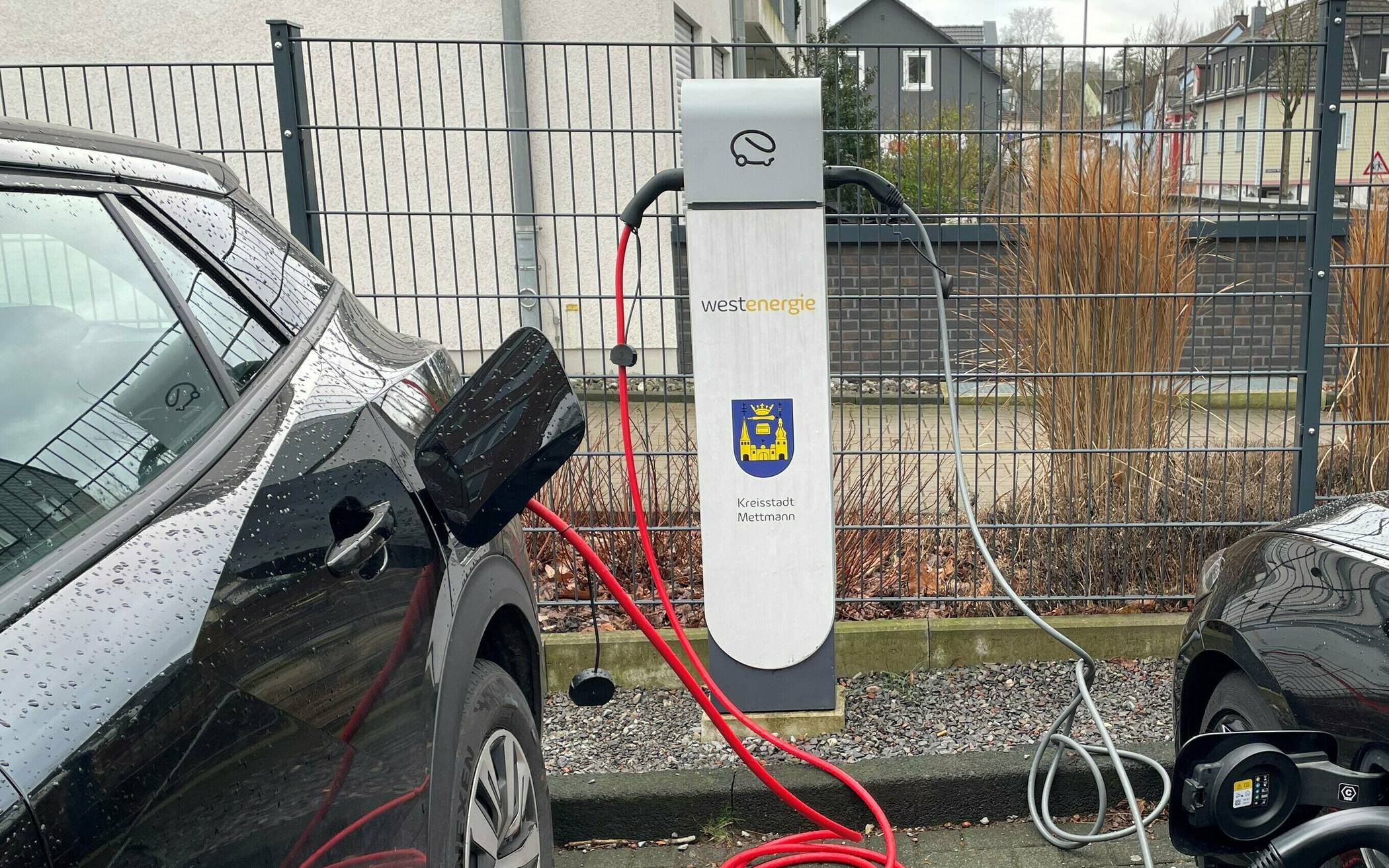 Zwei Elektroautos tanken Strom an der Ladesäule, die auf den Parkplatz neben dem Rathaus steht.   