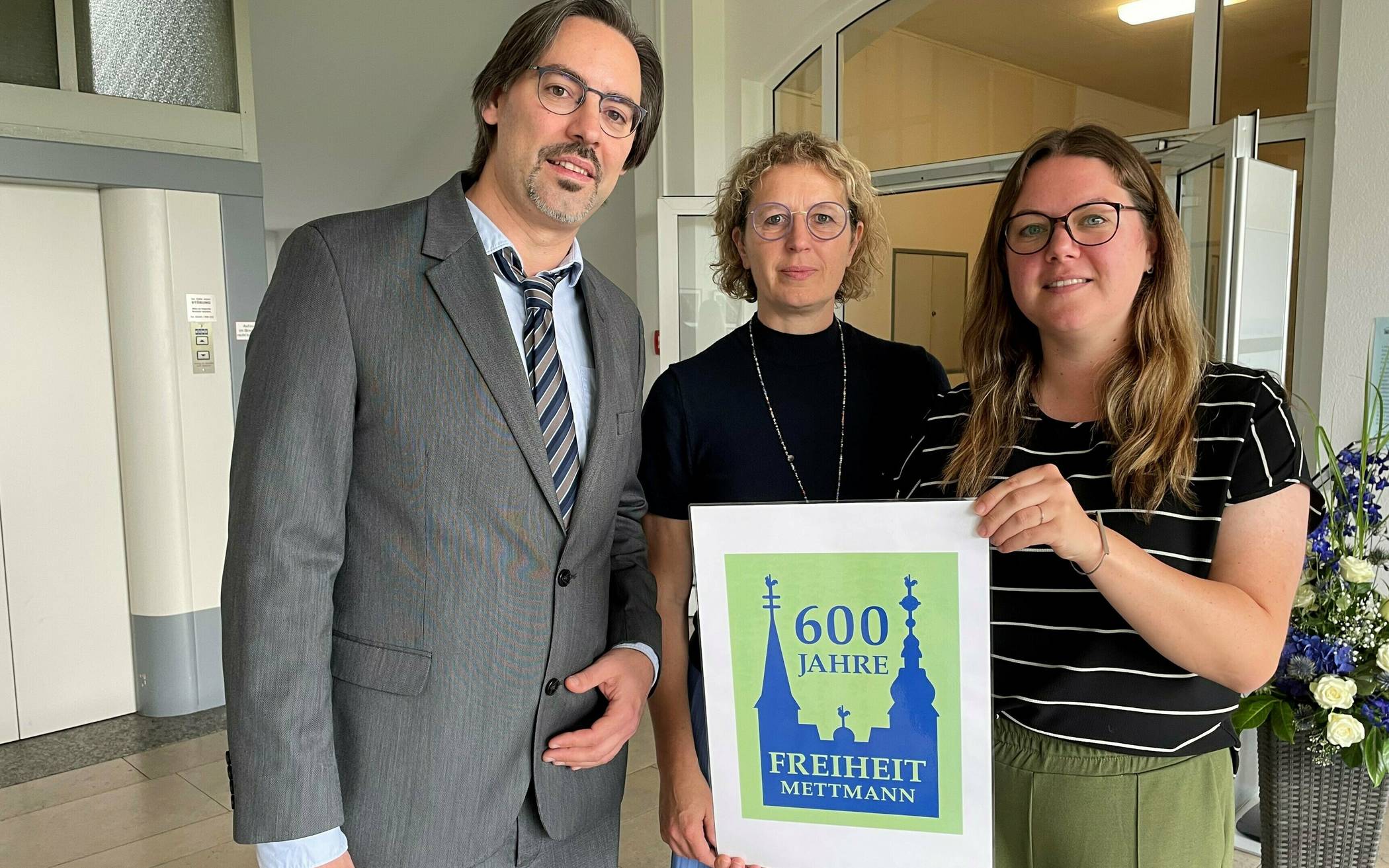 Bürgermeisterin Sandra Pietschmann, Anna Wagner (Kultur) und Stadtarchivar Marinko Betker präsentieren das Logo „600 Jahre Freiheit Mettmann“. 