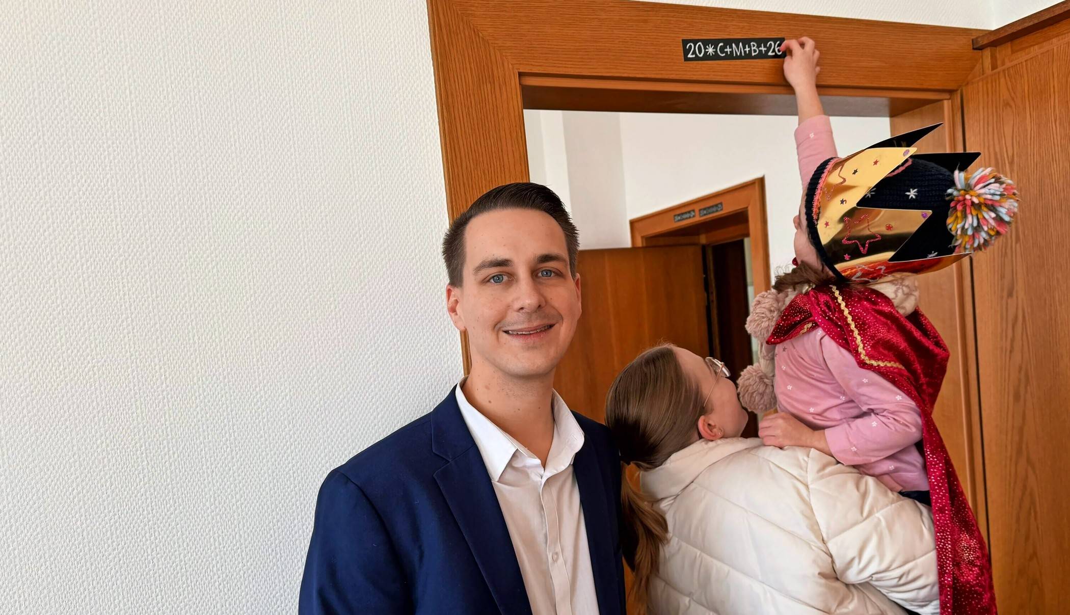  Ein Sternsinger wird hochgehoben, damit er den Segensspruch auf dem Türrahmen anbringen kann. 