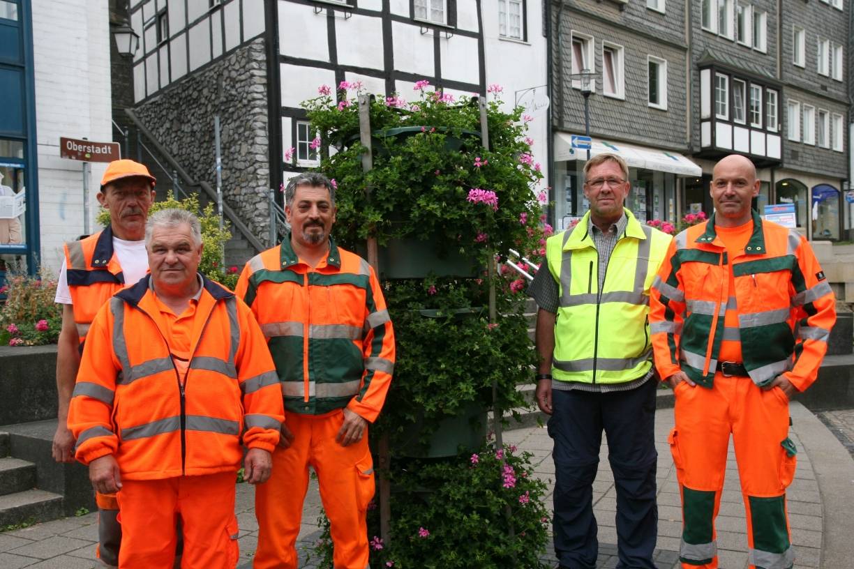  Sachgebietsleiter Thomas Gebhardt (gelbe Weste) mit den Mitarbeitern Peter Schroeder, Heinz Franken, Yasar Kilic, und Sven Kaeber (v. l.) an einer Blumensäule, die mit Geranien bepflanzt wurden. 