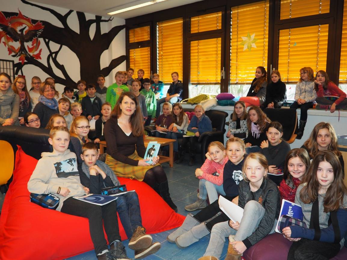  Kinderbuchautorin Petra Postert (Mitte) und Lehrerin Barbara Reh (hinten links, mit blauem Schal) mit Fünftklässlern in der KHG Bücherei. 